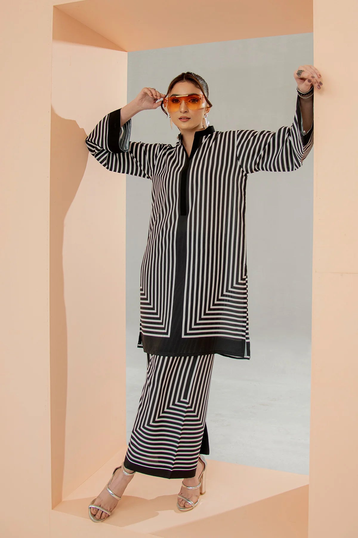 Woman wearing a black and white striped outfit with sunglasses in a minimalistic setting