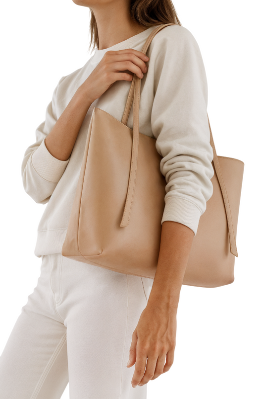 Beige tote bag held by a person wearing a light colored sweater and pants on a white background