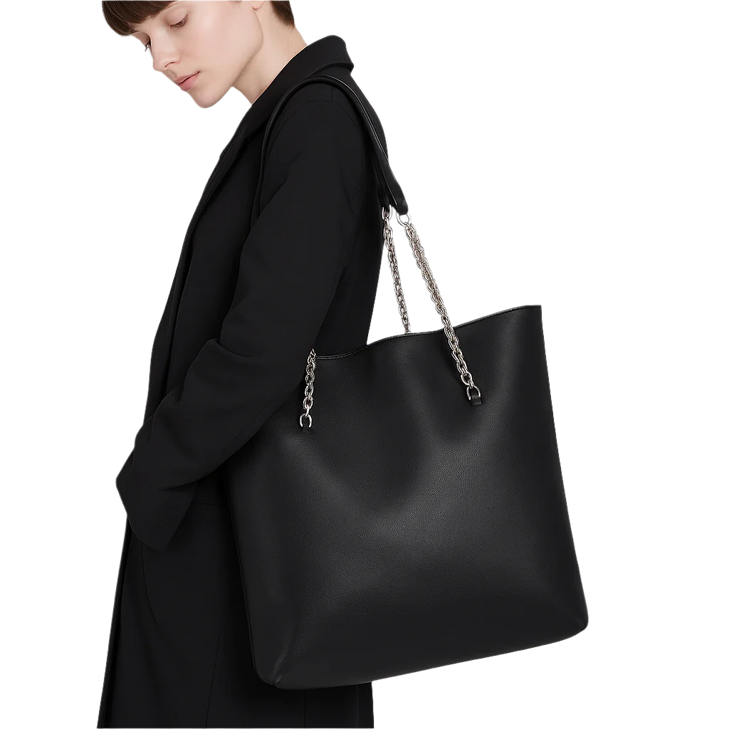 Person wearing a black coat with a large black handbag featuring a chain strap on a gray background