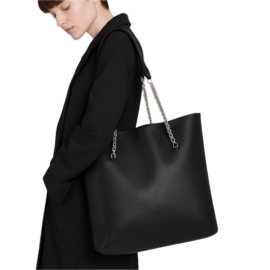 Person wearing a black coat with a large black handbag featuring a chain strap on a gray background