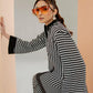Person wearing a black and white striped outfit with orange sunglasses against a light gray wall.