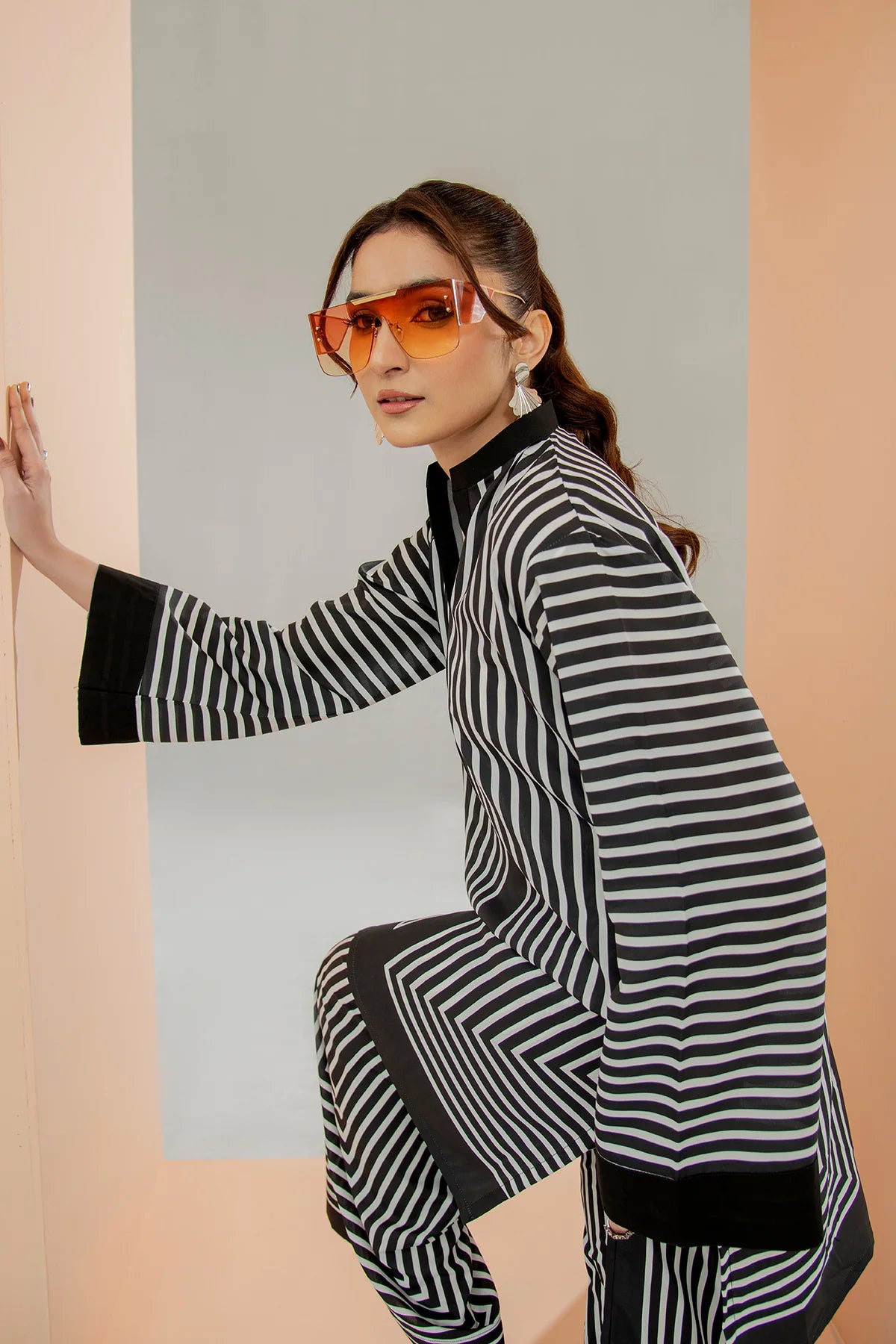Person wearing a black and white striped outfit with orange sunglasses against a light gray wall.