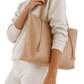 Beige tote bag held by a person wearing a light colored sweater and pants on a white background